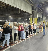 Group of individuals attentively listening to a speaker in a well-lit industrial space, suggesting an educational gathering.