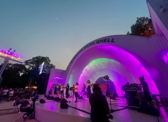 Vibrant outdoor concert scene with a band, colorful stage lighting, and an engaged audience enjoying the performance at twilight.