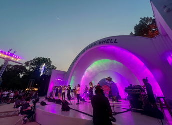 Vibrant outdoor concert scene with a band, colorful stage lighting, and an engaged audience enjoying the performance at twilight.