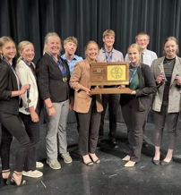 A smiling team on stage celebrates an achievement, holding a trophy, exuding joy, pride, and camaraderie in formal attire.