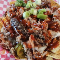 Plate of colorful nachos with shredded meat, barbecue sauce, green onions, and jalapeños on tortilla chips, evoking comfort.