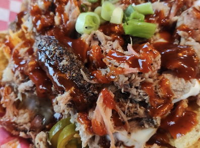 Plate of colorful nachos with shredded meat, barbecue sauce, green onions, and jalapeños on tortilla chips, evoking comfort.