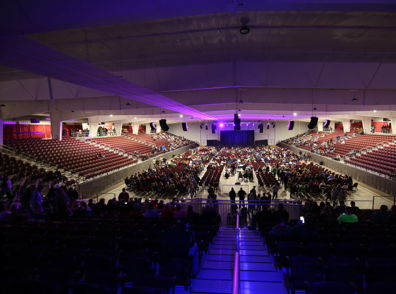 Indoor venue mostly empty, crowd gathered in front of a dimly lit stage, purple lighting creates an atmosphere of anticipation.