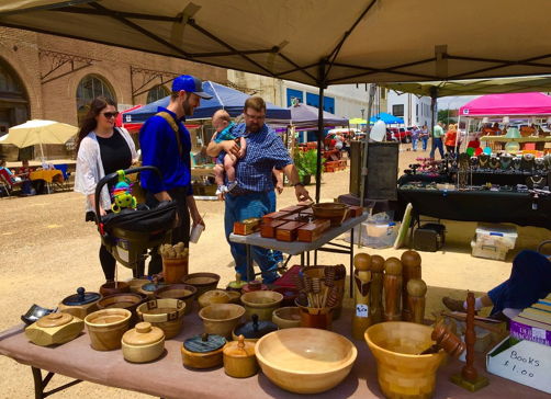 Outdoor market scene with vibrant handmade wooden items, a vendor, and families, evoking warmth and community.