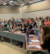 A lively lecture hall filled with engaged attendees focused on a presenter, creating a warm, inspiring atmosphere.