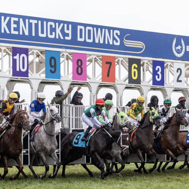 Horses burst from the starting gate at Kentucky Downs, showcasing vibrant jockey silks and capturing the thrill of the race.