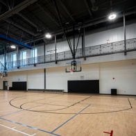Empty gymnasium with polished wood floor, basketball hoop, and bright natural light; evokes anticipation and possibility.