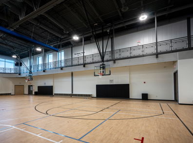 Empty gymnasium with polished wood floor, basketball hoop, and bright natural light; evokes anticipation and possibility.