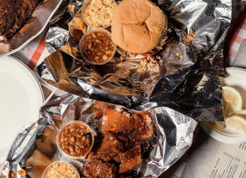 A cozy food spread with grilled meat, buns, and sides in foil, evoking warmth, comfort, and nostalgic picnic vibes.