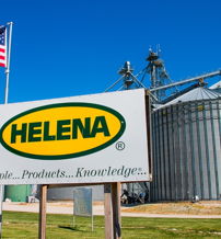 A bright blue sky features an American flag and a "HELENA" sign, highlighting agriculture and evoking community pride.