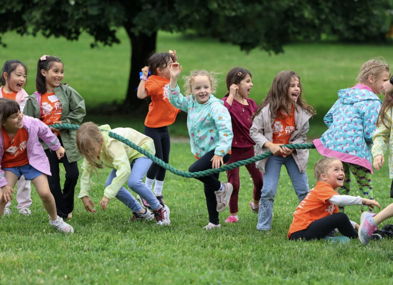 Children in bright orange shirts happily play tug-of-war outdoors, showcasing joy, teamwork, and the spirit of childhood.