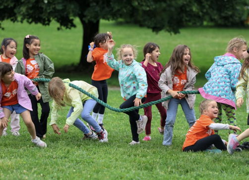 Children in bright orange shirts happily play tug-of-war outdoors, showcasing joy, teamwork, and the spirit of childhood.