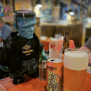 A whimsical table scene with a Frankenstein toy, beer, and festive decor, capturing a light-hearted, playful atmosphere.