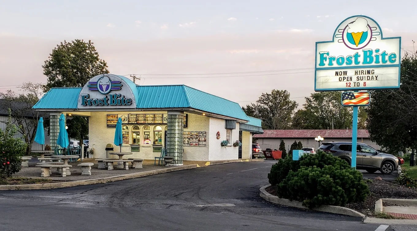 Quaint ice cream shop "Frost Bite" with a turquoise roof, outdoor seating, and a cheerful, inviting atmosphere.