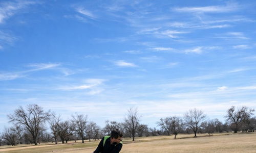 A golfer practices their swing at a range, focused under a clear blue sky, suggesting determination and enjoyment in nature.
