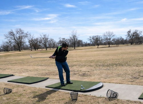 A golfer practices their swing at a range, focused under a clear blue sky, suggesting determination and enjoyment in nature.