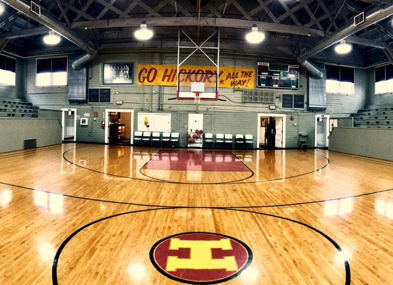 Indoor basketball court with polished wood, empty bleachers, and banners; evokes nostalgia and anticipation for future games.