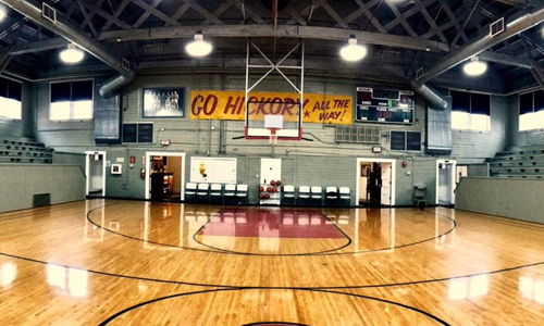 Indoor basketball court with polished wood, empty bleachers, and banners; evokes nostalgia and anticipation for future games.