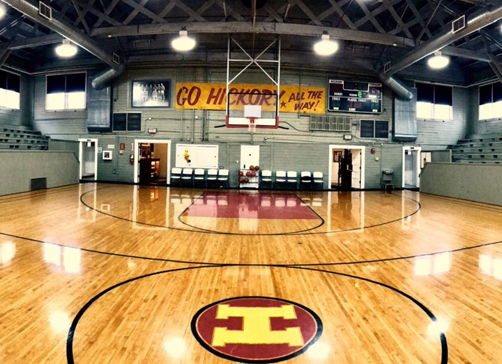 Indoor basketball court with polished wood, empty bleachers, and banners; evokes nostalgia and anticipation for future games.
