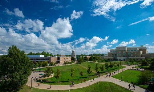 Vibrant campus with green lawns, trees, modern-traditional buildings, and people, evoking tranquility and student life.