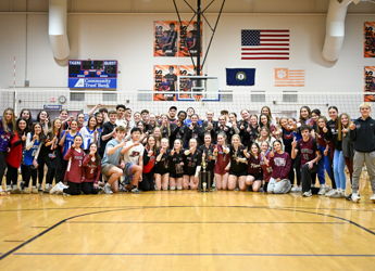 Celebration of volleyball players and supporters in a gym, posing with trophies, showcasing teamwork and joy.