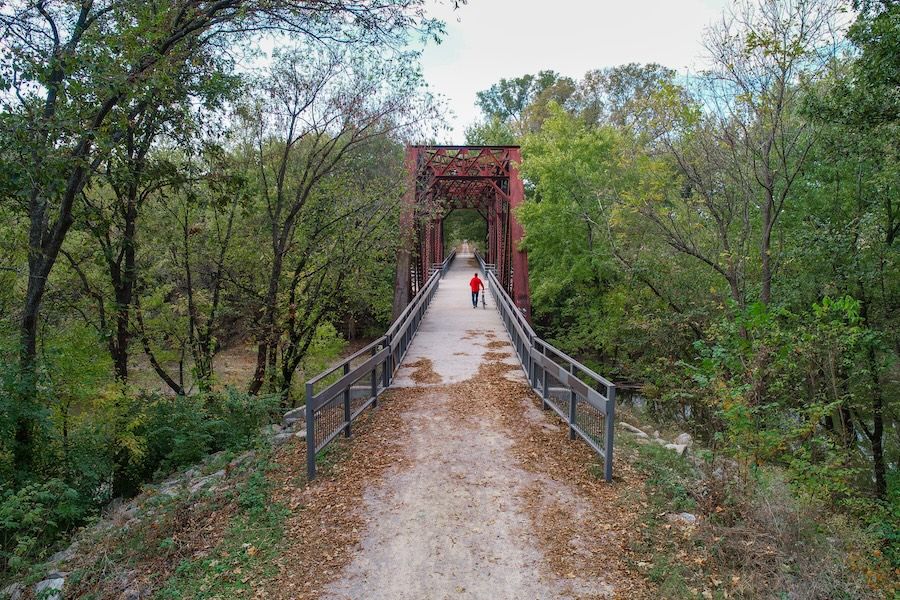 A person in red walks on a rustic bridge amid lush greenery, evoking tranquility and a sense of peaceful exploration.