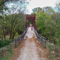 A person in red walks on a rustic bridge amid lush greenery, evoking tranquility and a sense of peaceful exploration.