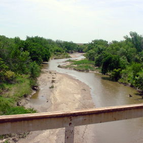 Serene landscape with a winding river, lush greenery, and tall trees, evoking peace and tranquility under a clear sky.