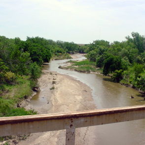 Serene landscape with a winding river, lush greenery, and tall trees, evoking peace and tranquility under a clear sky.