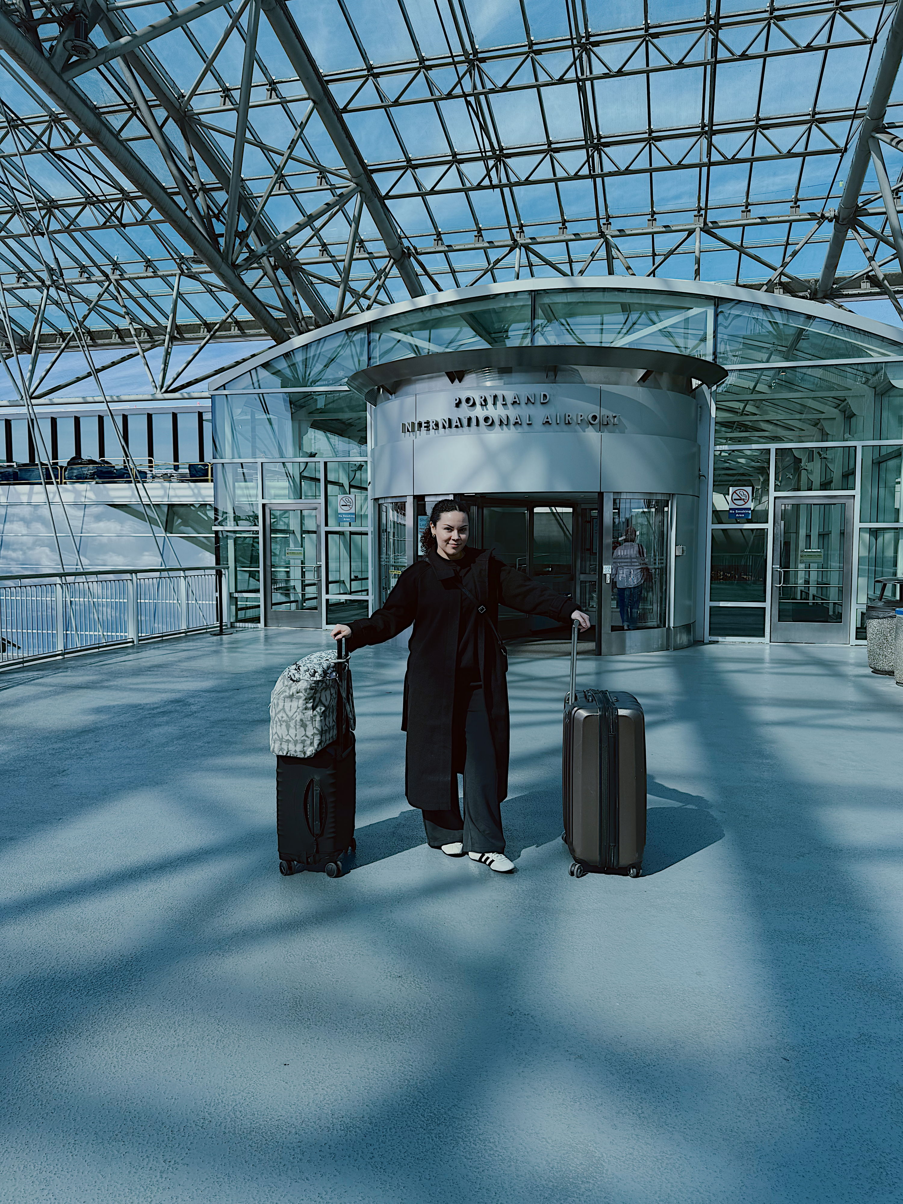 A person in a modern airport holds two suitcases, showcasing a minimalist design and evoking feelings of freedom and anticipation.
