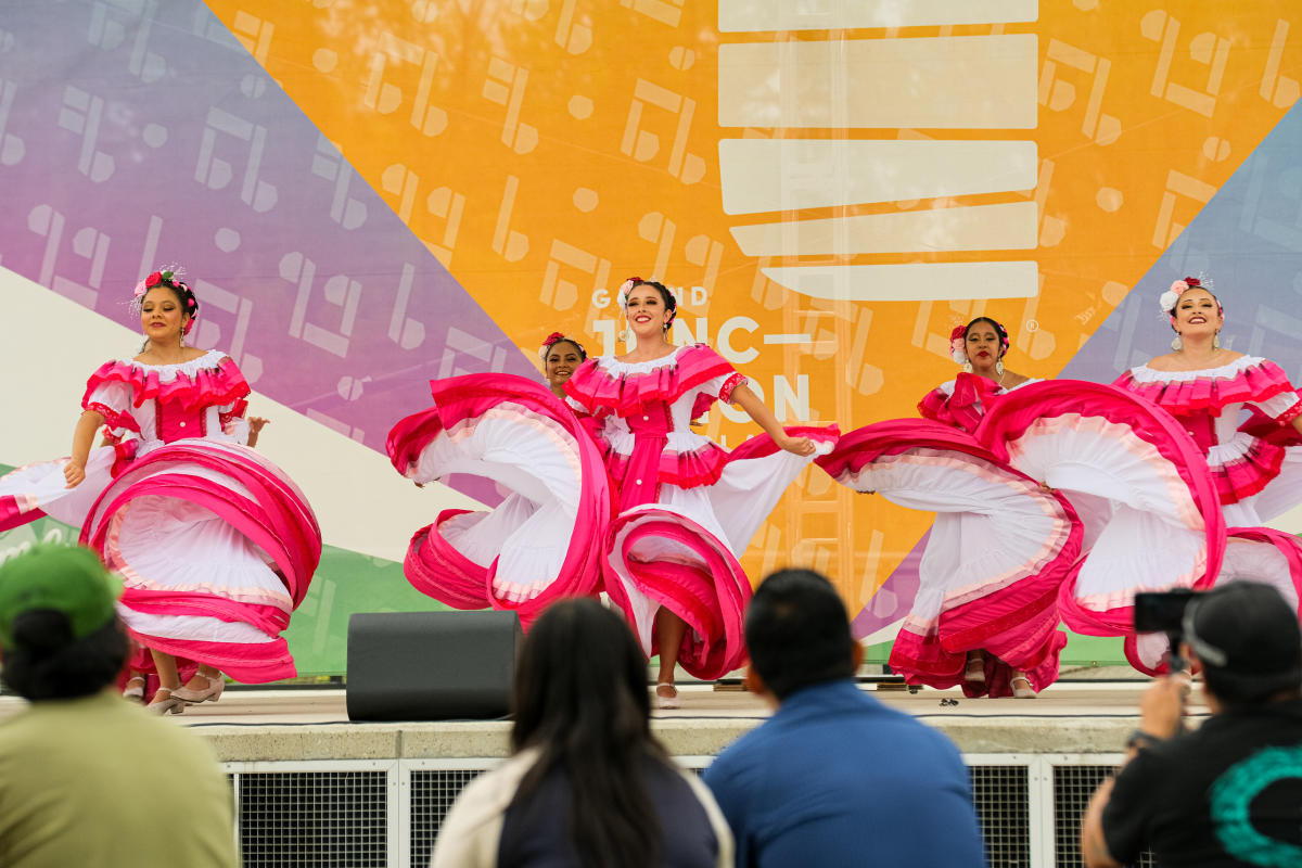 Vibrant performance with dancers in pink costumes, energetic on stage against a bright backdrop, engaging an attentive audience.