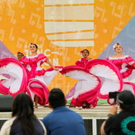 Vibrant performance with dancers in pink costumes, energetic on stage against a bright backdrop, engaging an attentive audience.