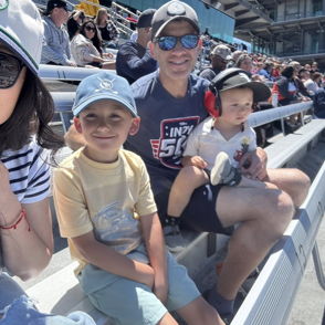 Family enjoying a sports event in grandstand seating, capturing smiles and joyful moments together in bright sunlight.