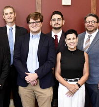 A group of eight people smiles together in a semi-formal setting, reflecting camaraderie and celebration.