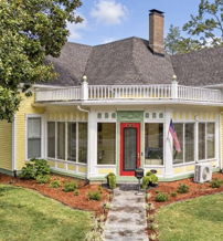 Charming yellow house with red door in a lush green setting evokes warmth, nostalgia, and a welcoming atmosphere.