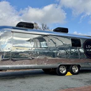 Shiny silver Airstream trailer branded "LOCAL HABIT," parked on a bright day, reflecting its surroundings with nostalgic charm.