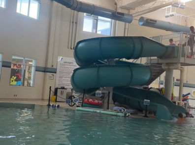 Indoor pool with turquoise slides, people swimming, and a pink float, creating a joyful, playful atmosphere for families.