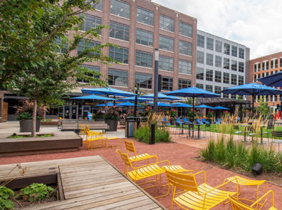 Vibrant outdoor space with modern architecture, blue umbrellas, yellow chairs, greenery, and a relaxing, inviting atmosphere.