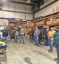 Group in a warehouse setting engaging in a professional training session, focused on a presentation with boxes and equipment around.