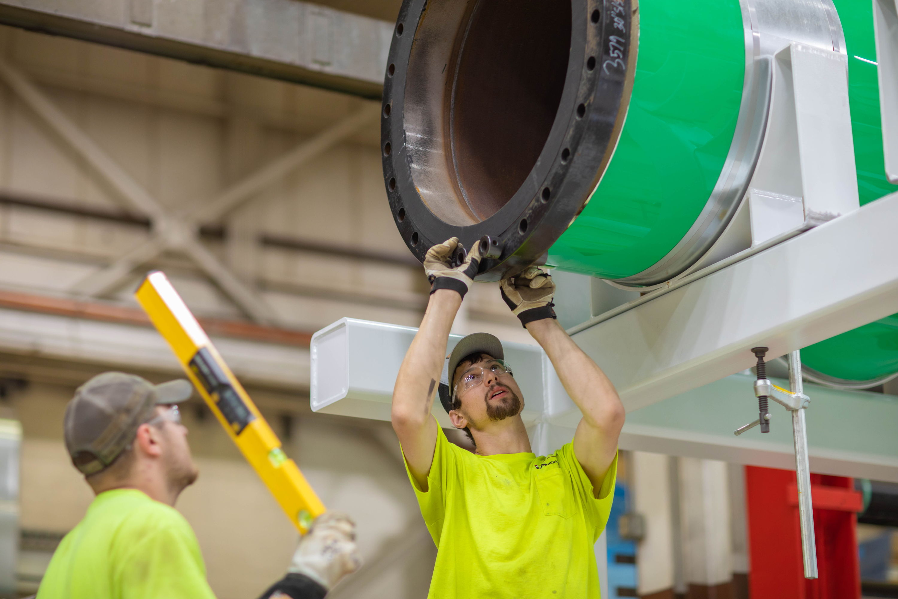 Two workers in bright yellow shirts collaborate on machinery, showing focus, determination, and a strong work ethic.