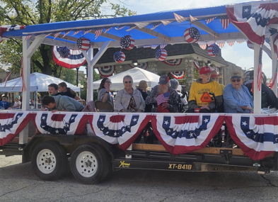 A festive, decorated trailer with people celebrating, featuring red, white, and blue bunting, exuding joy and community spirit.