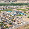 Aerial view of a serene suburban area with turquoise-roofed buildings, houses, green spaces, and hills in the background.