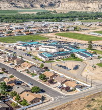 Aerial view of a serene suburban area with turquoise-roofed buildings, houses, green spaces, and hills in the background.