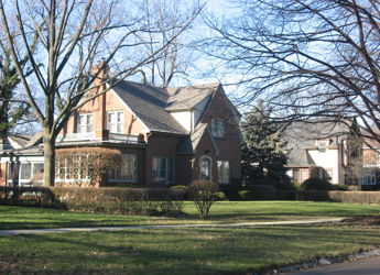 A charming brick house with a steep roof, surrounded by a manicured yard, evokes warmth and nostalgia in a serene setting.