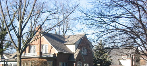 A charming brick house with a steep roof, surrounded by a manicured yard, evokes warmth and nostalgia in a serene setting.
