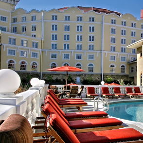 Elegant outdoor pool area with clear blue water, red lounge chairs, and light-colored buildings, evoking relaxation and luxury.