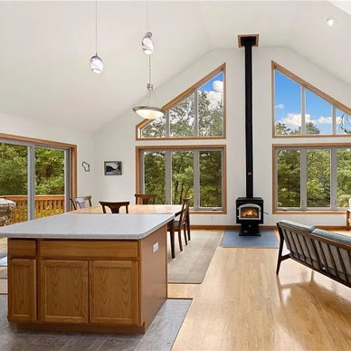 Bright, spacious living area with large windows, modern design, cozy seating, stylish wood stove, warm colors for comfort.