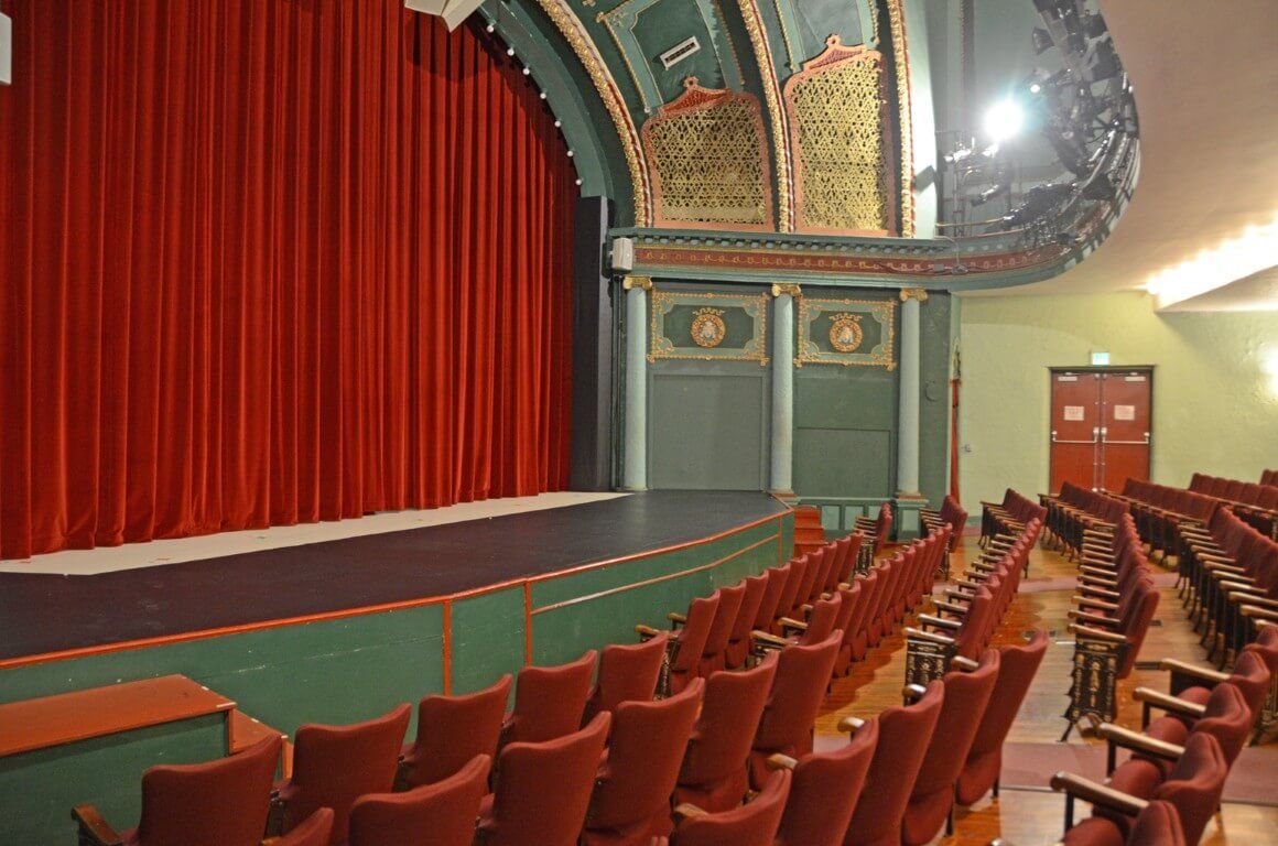 Classic theater interior with red curtain, inviting seating, and ornate decor, evoking excitement and nostalgia.