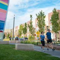 A vibrant outdoor scene with a couple jogging, lush greenery, modern buildings, and a colorful sculpture, evoking vitality and wellness.