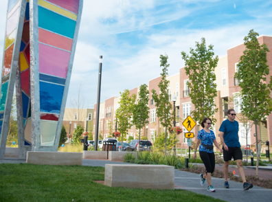 A vibrant outdoor scene with a couple jogging, lush greenery, modern buildings, and a colorful sculpture, evoking vitality and wellness.
